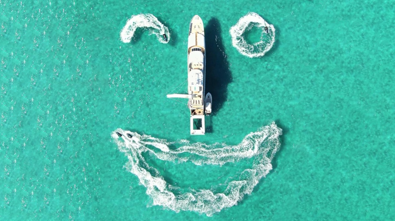 superyacht Loon viewed from above with a smile drawn by jet skis on the sea